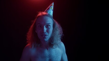 Portrait of crazy happy man with long hair, surfer male celebrating birthday, looking widely smiling, creepy halloween dark background. 