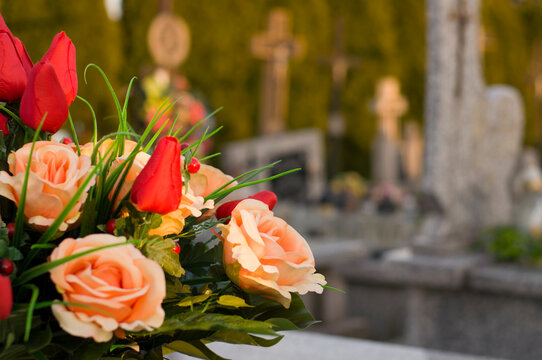 A tomb decorated with candles and flowers with cementary in the background.