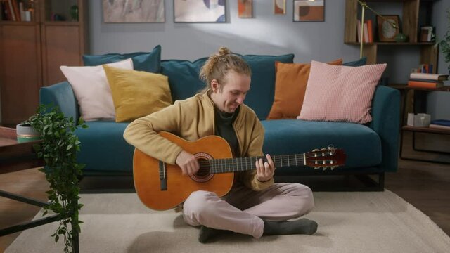 Happy man playing acoustic guitar sitting on floor, dinamic fast song. Creative hobby. Blogger Teacher teaching how to play on music instrument online. Remote musical learning. 
