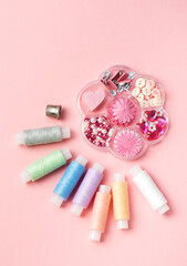 Set.for sewing and handicraft: colorful spools thread, buttons, thimble, rhinestones and beads on a pink background, top view