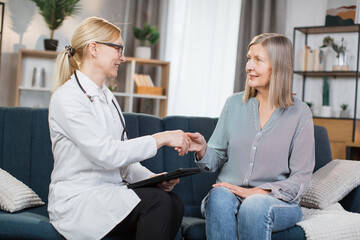 Pleasant confident skilled blond woman doctor in glasses and white coat, visiting patient, senior...