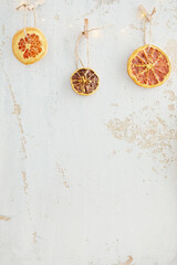 Background with dried oranges hanging on a craft rope with clothespins and LED garland on a light background of cracked paint on plywood. Eco jewelry concept for New Year and Christmas.