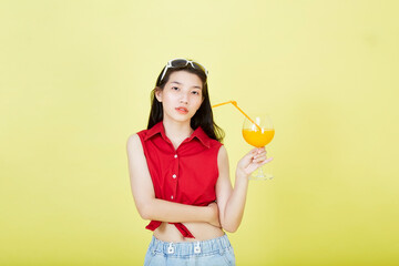Beautiful cute happy Asian hair brunette woman in summer casual clothes with a glass of fresh fruit juice drink studio shot isolated on colorful a yellow background