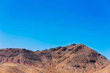 Reddish brown barren mountain peak under bright blue sky.