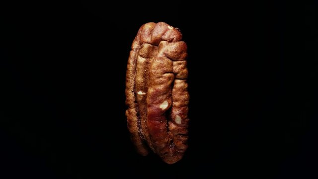 The peeled pecans are spinning. Close-up. Black background, side view.
