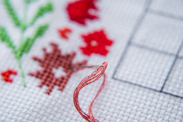 Close-up of cross-stitch. A Needle with thread is stuck in the canvas. Piece of embroidery