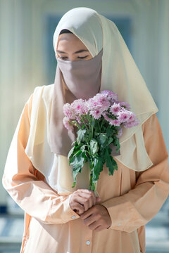 Beautiful Muslim woman in traditional dress, covering her face with a scarf, holding a bouquet