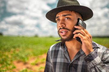 Latin American farmer working on plantation. Young man talking on cellphone, wearing hat