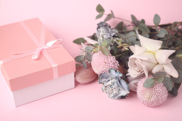 Pink gift box and a bouquet of different flowers in pink tones on a pink background.