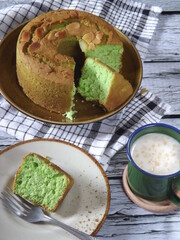Whole cake with Slices of Pandan sponge cake or bolu pandan, Indonesian traditional Pandan cake topped with canary slices, served on plate with cup of milk. Also known as chiffon cake.