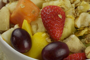 Fruit salad with chestnuts and granola in a bowl. Multicolored ripe fruits. Pineapple, mango, grape, strawberry, papaya, melon, banana and kiwi..