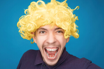 Funny portrait of a man with happy emotion on his face in the studio on blue background. Man wearing wig. Yellow hair