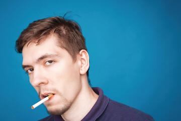 Handsome young man smoking cigarette. one caucasian stylish man smoking cigarettes portrait on blue background