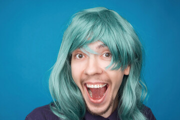Funny portrait of a man with happy emotion on his face in the studio on blue background. Man wearing wig. Green hair