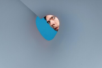 Man looking inside rounded tube. Close-up shot of shocked young man with round eyes