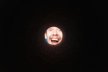 Man looking inside rounded tube. Close-up shot of happy shocked young man with round eyes and open mouth  smile.