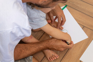 PAI E FILHO DESENHANDO EM UMA FOLHA DE PAPEL, SENTADOS NO CHÃO.
