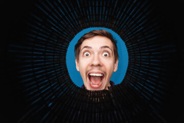 Man looking inside rounded tube. Close-up shot of happy shocked young man with round eyes and open mouth  smile.