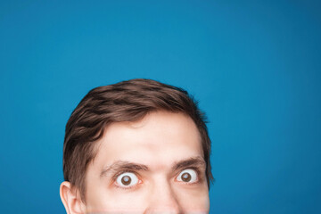 Man's eyes looking up on the light background. Empty place for a text or object. Close-up shot of shocked young man with round eyes, top half head. Eyes looking on front