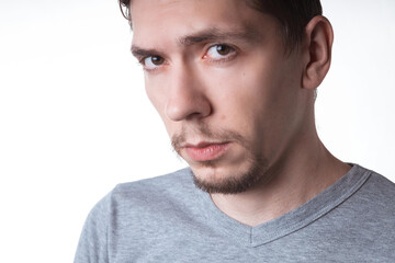 Obraz premium Portrait of a sensual young model in unlabeled gray t-shirt posing on white background. Serious man with small beard close-up portrait