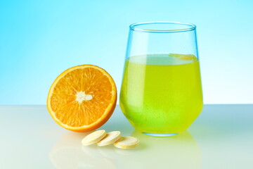 Fototapeta na wymiar effervescent vitamin C pill dissolves in water. a glass of water, effervescent pill and orange on blue background. vitamin C concept