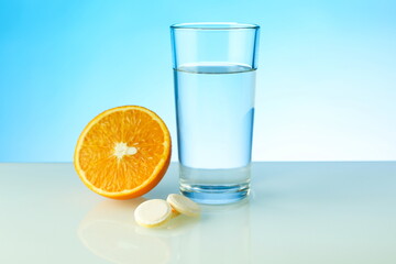 a glass of water, effervescent pill and orange on blue background with copy space. vitamin C concept. biologically active food supplement