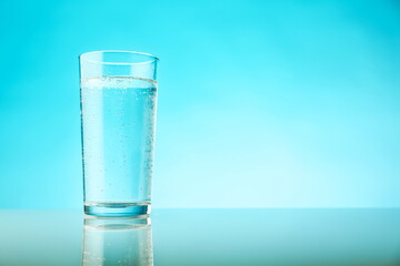 glass of sparkling water on blue background with copy space. mineral water with gas bubbles in a glass on a light blue background