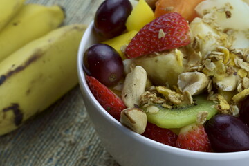 Fruit salad with chestnuts and granola in a bowl. Multicolored ripe fruits. Pineapple, mango, grape, strawberry, papaya, melon, banana and kiwi..