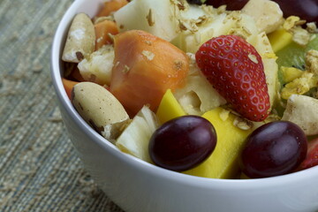 Fruit salad with chestnuts and granola in a bowl. Multicolored ripe fruits. Pineapple, mango, grape, strawberry, papaya, melon, banana and kiwi..