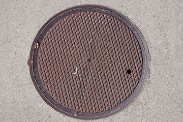 Close-up view of a small iron cover plate for a water or sewer valve in the asphalt of a city street
