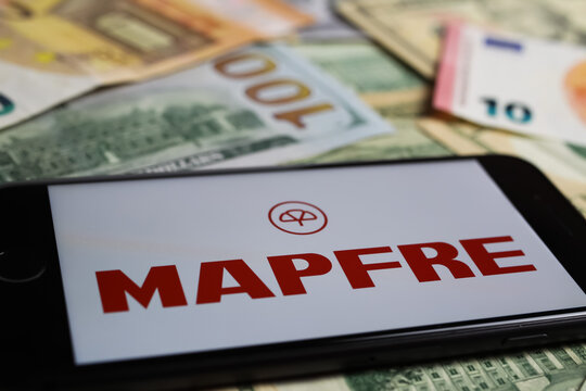 Viersen, Germany - March 1. 2021: Closeup of smartphone with logo lettering of mapfre seguros insurance company on paper money currency