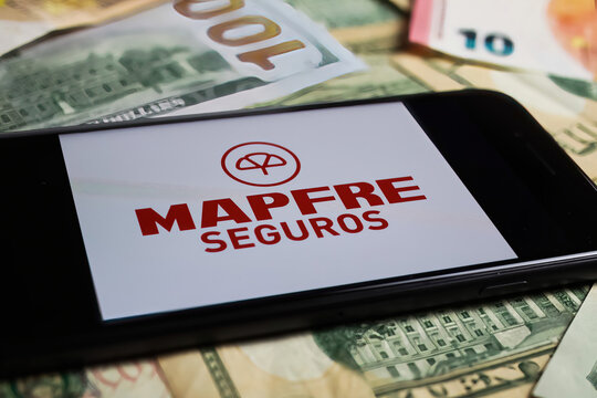 Viersen, Germany - March 1. 2021: Closeup of smartphone with logo lettering of mapfre seguros insurance company on paper money currency