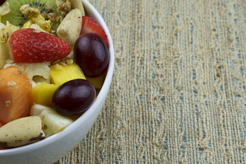 Fruit salad with chestnuts and granola in a bowl. Multicolored ripe fruits. Pineapple, mango, grape, strawberry, papaya, melon, banana and kiwi..