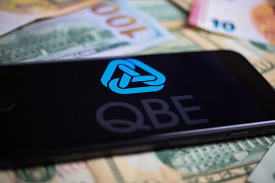 Viersen, Germany - March 1. 2021: Closeup of smartphone with logo lettering of australian qbe insurance company on paper money currency