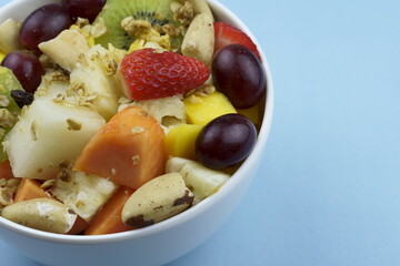 Fruit salad with chestnuts and granola in a bowl. Multicolored ripe fruits. Pineapple, mango, grape, strawberry, papaya, melon, banana and kiwi..