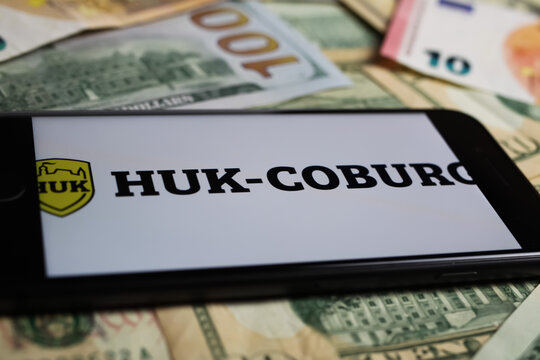 Viersen, Germany - March 1. 2021: Closeup of smartphone with logo lettering of huk coburg insurance company on paper money currency