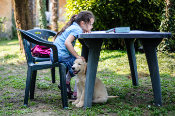 A little girl reading book with little puppy in garden