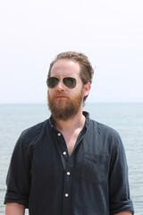 portrait of attractive man 30s with beard ocean sea behind him on sunny day 