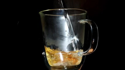 A bag of tea in a transparent mug is watered with hot water.