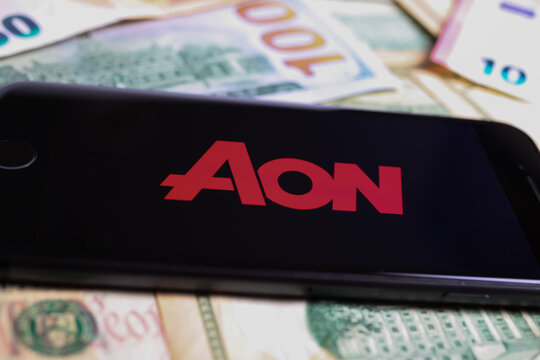 Viersen, Germany - March 1. 2021: Closeup of smartphone with logo lettering of aon insurance company on paper money currency