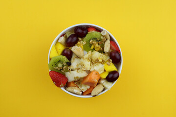 Fruit salad with chestnuts and granola in a bowl. Multicolored ripe fruits. Pineapple, mango, grape, strawberry, papaya, melon, banana and kiwi. Top view.