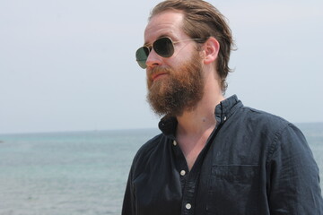 portrait of attractive man 30s with beard ocean sea behind him on sunny day in navy shirt