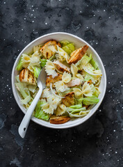 Caesar pasta salad in a bowl on a dark background, top view. Delicious lunch, snack