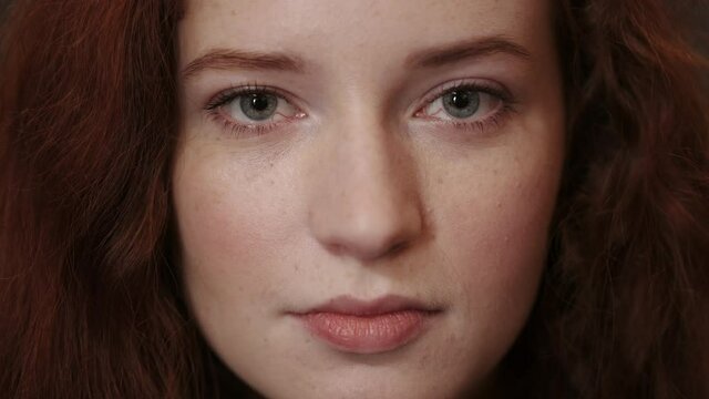 Close up view of young red haired woman face looking to camera. Portrait of beautiful female person with blue eyes posing. Concept of headshot.