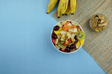 Fruit salad with chestnuts and granola in a bowl. Multicolored ripe fruits. Pineapple, mango, grape, strawberry, papaya, melon, banana and kiwi. Top view.