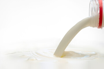 pouring milk to the surface from a plastic bottle on a white background