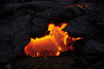 Magma or melted lava flowing through hardened lava glowing from heat and burn. Created in the...