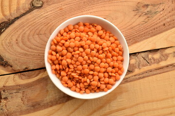 Red organic, uncooked lentils in a white dish on a wooden table, close-up, top view.