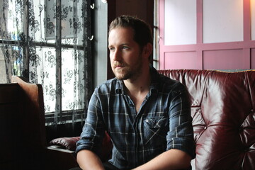 attractive male in blue plaid shirt   relaxed and confident in living room sitting 