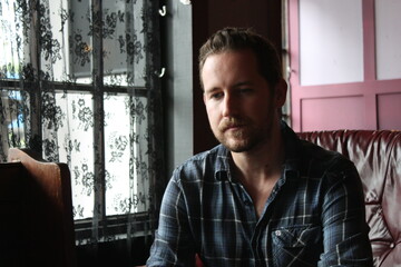 attractive male in blue plaid shirt   relaxed and confident in living room sitting 